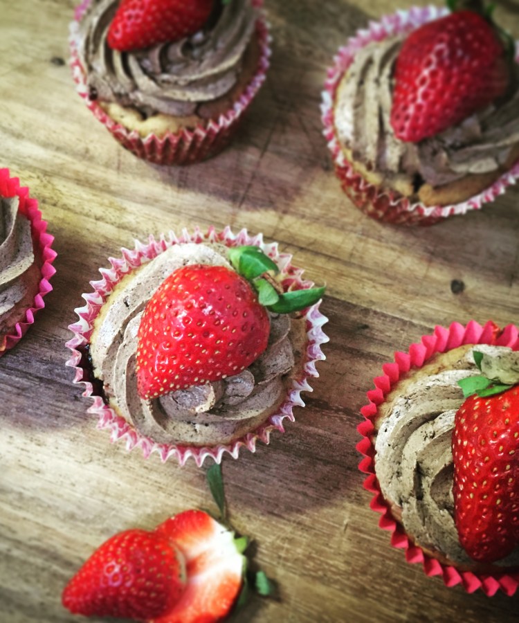 A selection of berry muffins topped with berry icing and strawberries.