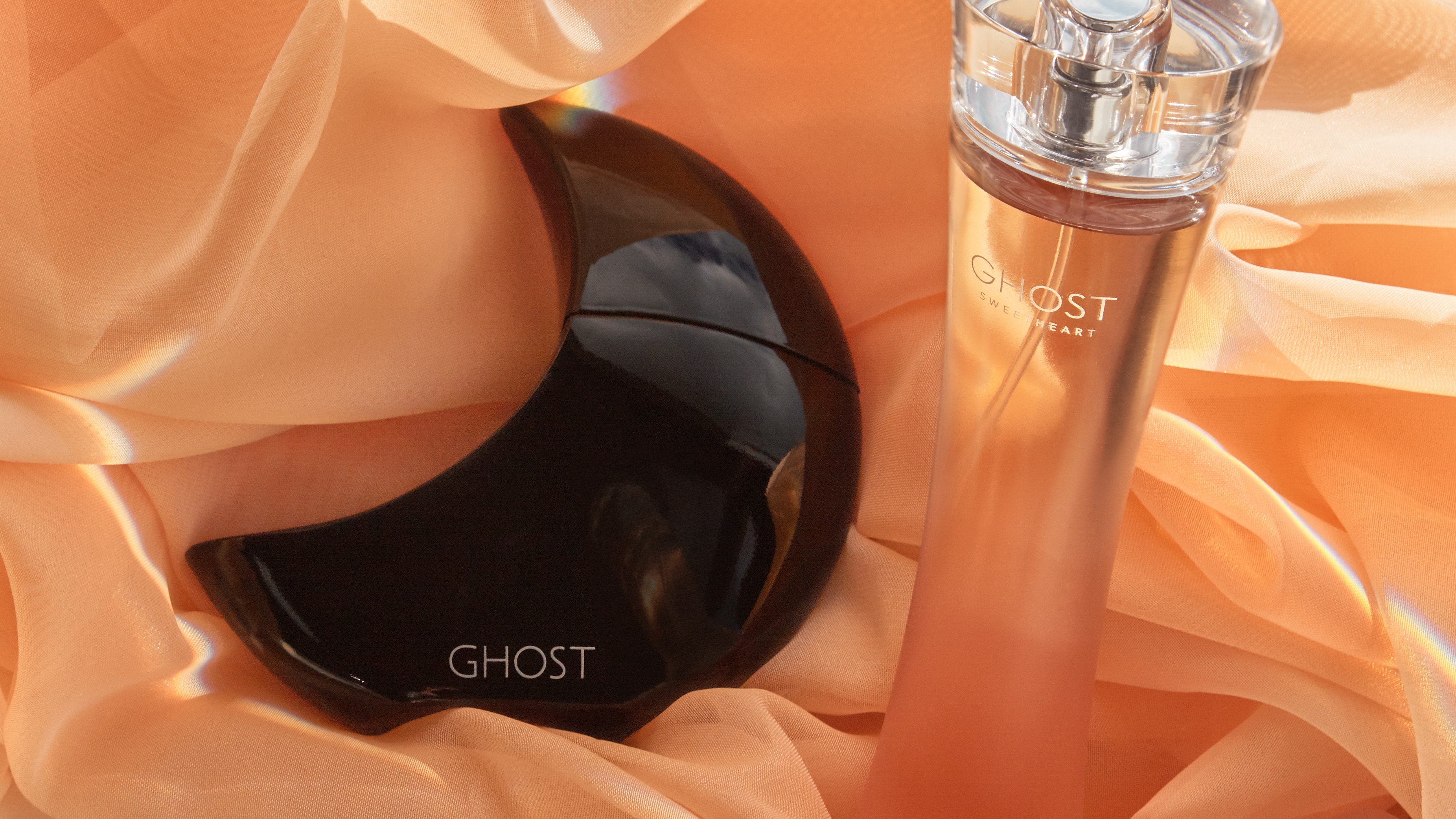 Two GHOST perfumes against a soft peach coloured fabric background